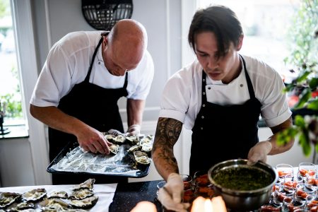Chef needed in Oxford Two chefs in a restaurant kitchen preparing gourmet dishes with fresh ingredients and focused expressions.