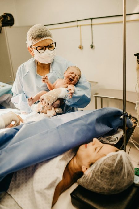A doctor holds a newborn baby in a hospital setting post-delivery.