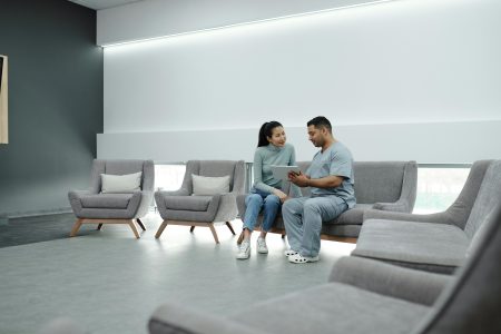 Healthcare Assistant needed in Dorset (Visa Sponsorship Available) A doctor in scrubs consulting a female patient in a modern clinic waiting room, using a tablet.