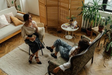 Consultant Psychiatrist needed in Exeter (Visa Sponsorship Available) Two women engaged in a psychotherapy session in a warm, inviting interior with plants and natural lighting.