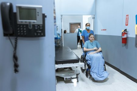Healthcare Assistant needed in Midhurst (Visa Sponsorship Available) A nurse helps a patient in a wheelchair down a hospital corridor, reflecting care and medical professionalism.