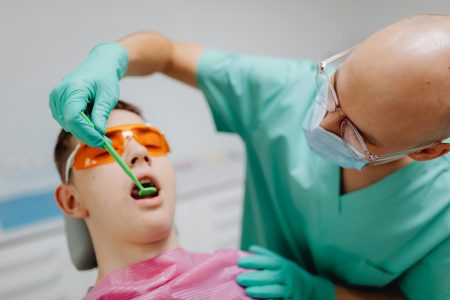A dentist conducts a dental checkup on a teenage patient wearing protective eyewear.