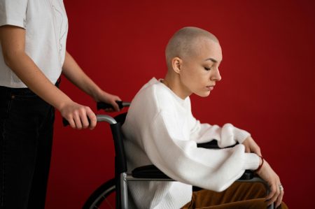 Young woman in wheelchair with shaved head reflecting in a studio with red background.