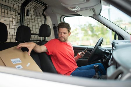 Delivery Driver needed in Southampton Man in red shirt handling package inside delivery van, holding phone.
