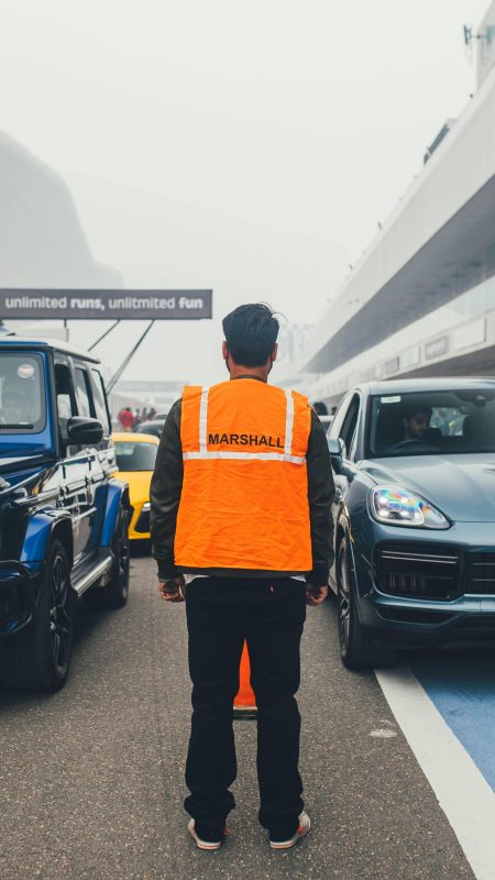 Marshall in orange vest directing cars on a foggy racing circuit.