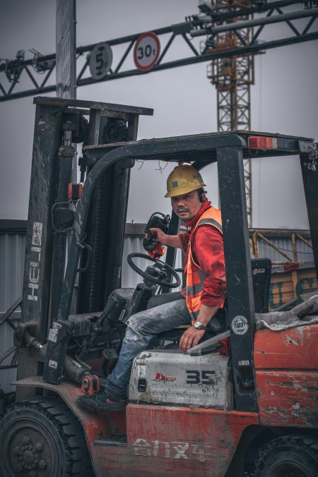 Forklift Driver needed in Ipswich A construction worker wearing a safety helmet operates a forklift on-site under a crane.