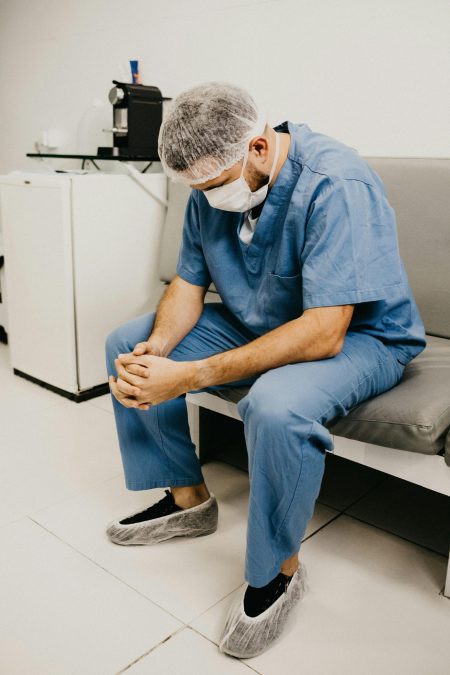 Healthcare Assistant needed in Wellington (Visa Sponsorship Available) A male doctor in hospital attire sitting pensively, representing healthcare challenges.