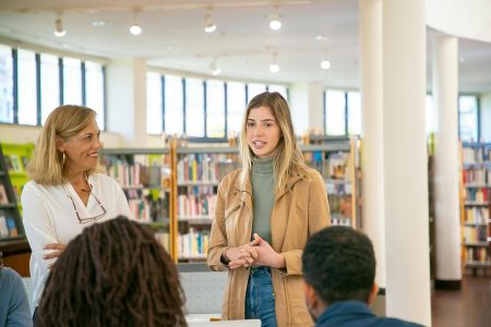 Students and teacher engaged in an active discussion inside a bright university library.