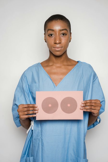 Woman in medical gown holding breast cancer awareness card symbol, promoting health care education.