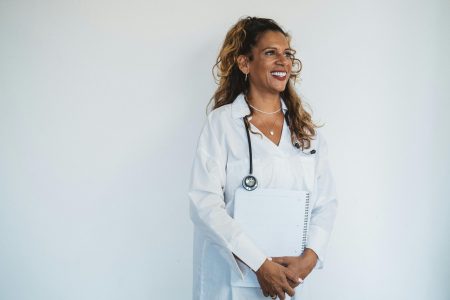 Confident female doctor in a white coat smiling while holding a notebook.
