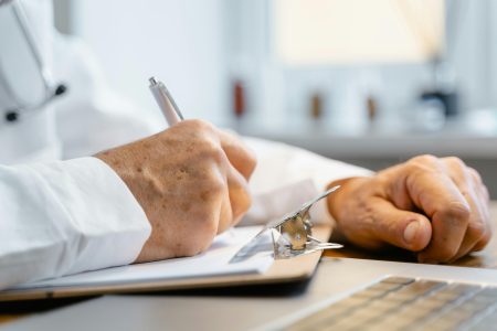 Close-up of a doctor writing notes on a clipboard in a well-lit office.