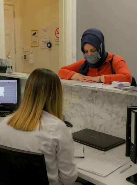 Patient visiting a medical office reception, discussing appointment details with receptionist.