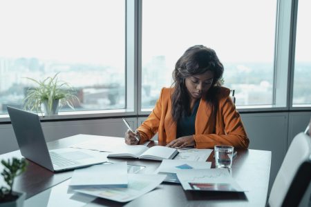 Project Management Office Director needed in UK (Remote) Focused black businesswoman analyzing documents at an office desk with city view.