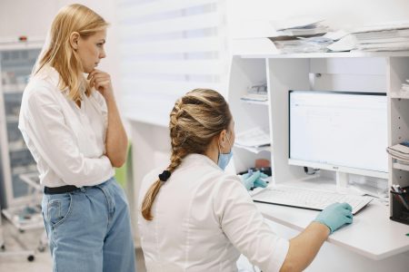 Healthcare Data Entry Specialist needed in Nigeria (Remote) Two female healthcare workers collaborate in a clinic, analyzing data on a computer screen.