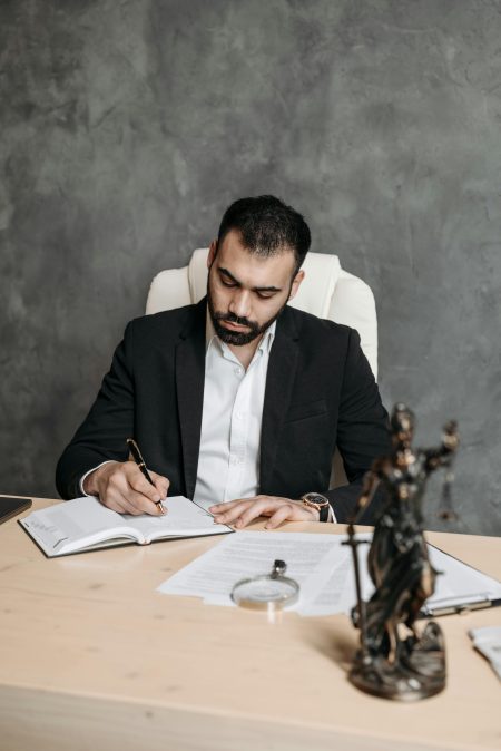 Professional lawyer in a suit taking notes at a desk with legal documents and statue.