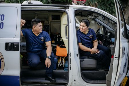 Two paramedics sitting in an ambulance, taking a break and smiling while in uniform.