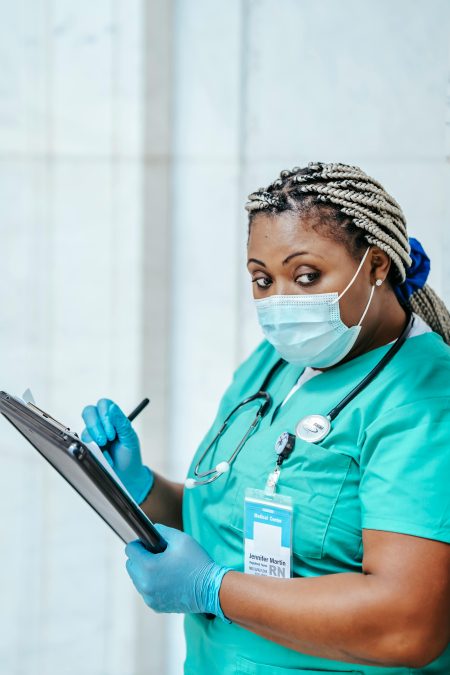 Professional nurse with protective gear reviewing notes on clipboard in a medical environment.