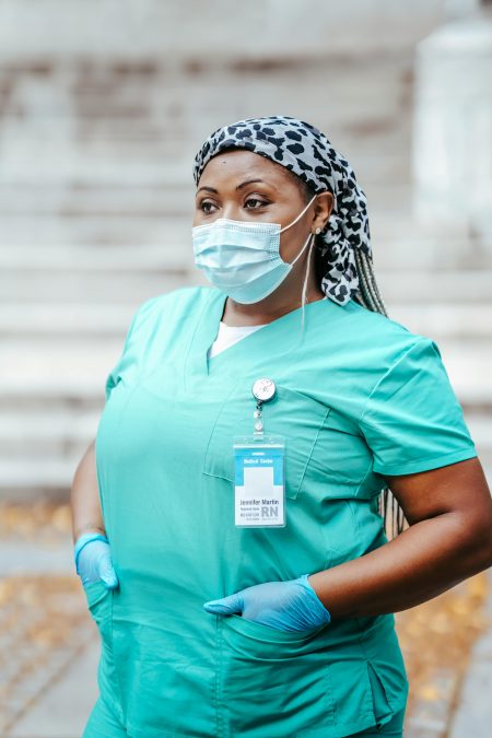 A confident female medic wearing a mask and uniform standing outdoors.