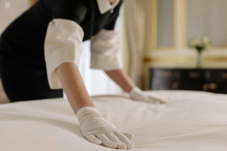 Housekeeper needed in Gloucester A housekeeper straightening the bed linens in a well-appointed hotel room.