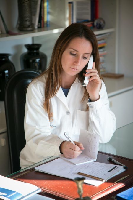 Female doctor in a white coat taking notes while on a phone call, symbolizing multitasking and professionalism.