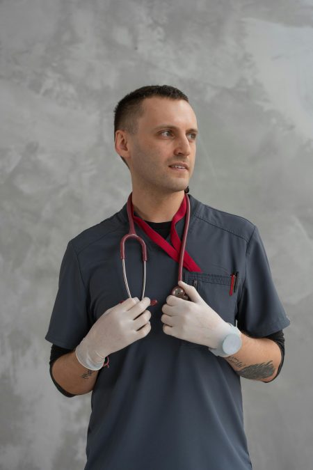 Male doctor in gray scrubs and latex gloves looking sideways against a gray background.