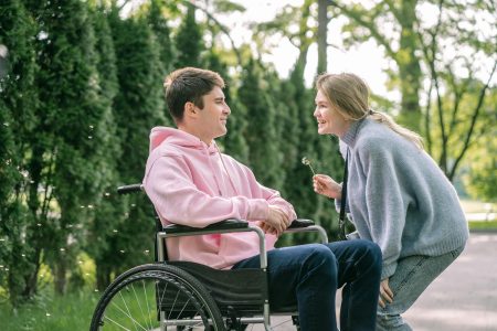 A young man in a wheelchair enjoys a cheerful moment with a woman outdoors.