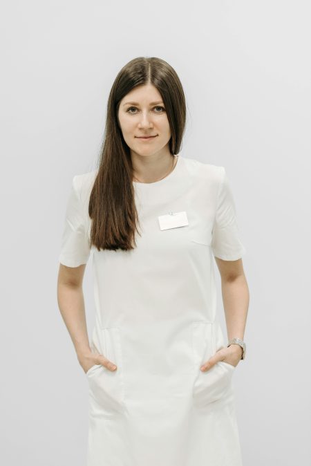 Professional nurse posing in a white uniform indoors on a plain background.