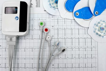 Specialist Cardiac Physiologist/Healthcare Scientist needed in Manchester (Visa Sponsorship Available) Close-up of ECG device with leads and electrodes on printed heart rate graph, showcasing medical technology.