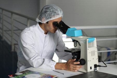 Head of Population Health Sciences needed in London (Visa Sponsorship Available) Scientist in a lab coat using a microscope to conduct research, focusing on healthcare improvements.
