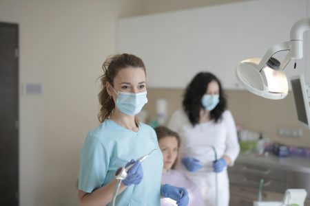 A dentist in a modern clinic attending to a patient with assistant present.