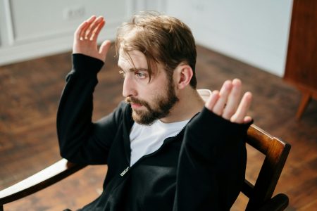 Senior Mental Health Nurse needed in London (Visa Sponsorship Available) Bearded man sitting and gesturing expressively in a well-lit interior space.