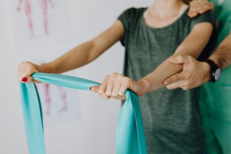 Occupational Therapist needed in Great Yarmouth (Visa Sponsorship Available) Crop unrecognizable orthopedist in uniform and wristwatch supporting shoulder and reached arm of faceless female patient with resistance band in doctor office