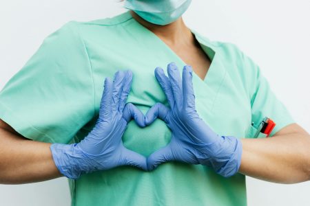Medical professional forming a heart shape with blue gloves. Symbol of care and compassion.