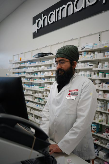 Senior Specialist Pharmacist needed in Southampton (Visa Sponsorship Available) Asian male pharmacist in a lab coat working at a pharmacy counter with shelves of medicine.