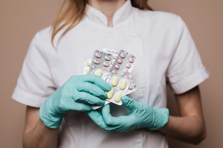 Clinical Pharmacist needed in Hackney (Visa Sponsorship Available) Close-up of a healthcare professional wearing gloves and holding blister packs of medication.