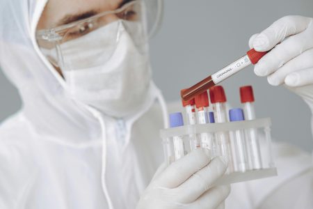 Healthcare Scientist needed in Southampton (Visa Sponsorship Available) Scientist wearing PPE works in lab holding coronavirus test tube with focused concentration.