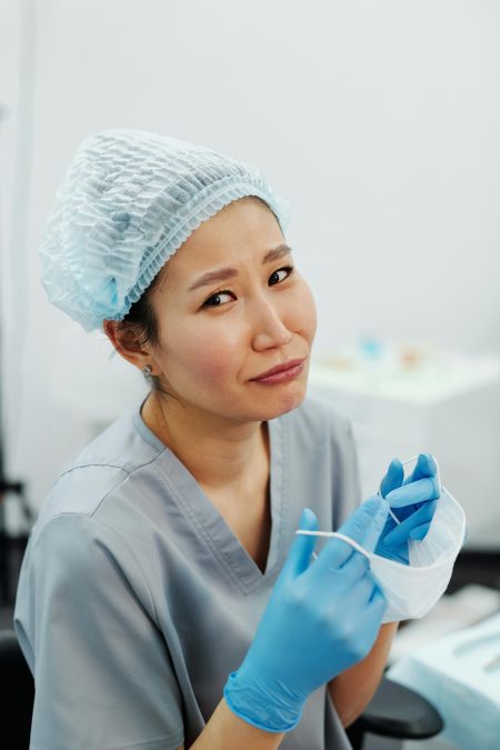 Nursing Associate needed in Watford (Visa Sponsorship Available) Asian nurse in scrubs and protective gear getting ready for work indoors.