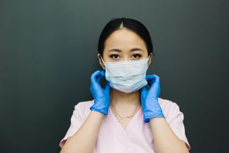 Portrait of a healthcare worker adjusting a face mask, wearing gloves.