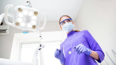 Orthodontic Therapist needed in Sidcup (Visa Sponsorship Available) From below view of female dentist in medical uniform wearing mask and protective eyeglasses and latex gloves with dental mirror while preparing for examination of patient