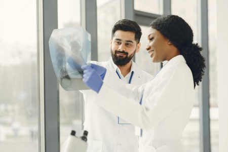 Consultant Radiologist in Vascular needed in Leicester (Visa Sponsorship Available) Two doctors in lab coats examine an X-ray image in a bright medical facility.