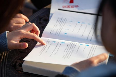 Hands pointing and reading a book with text. Outdoor educational activity.