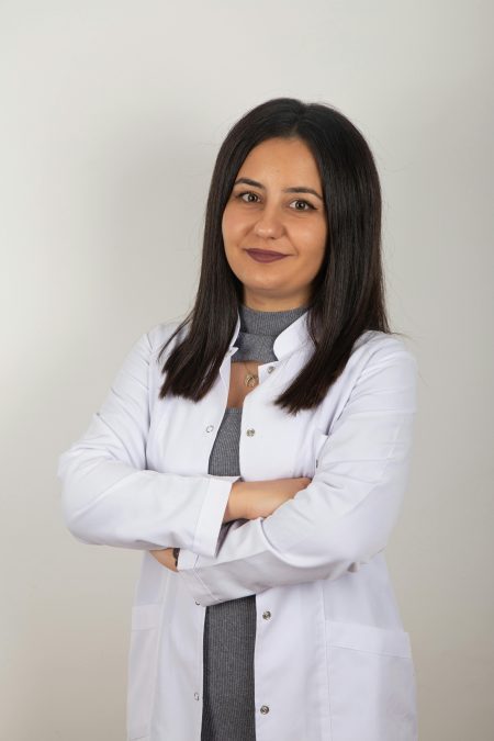 Portrait of a confident female doctor in a white coat standing against a plain background.