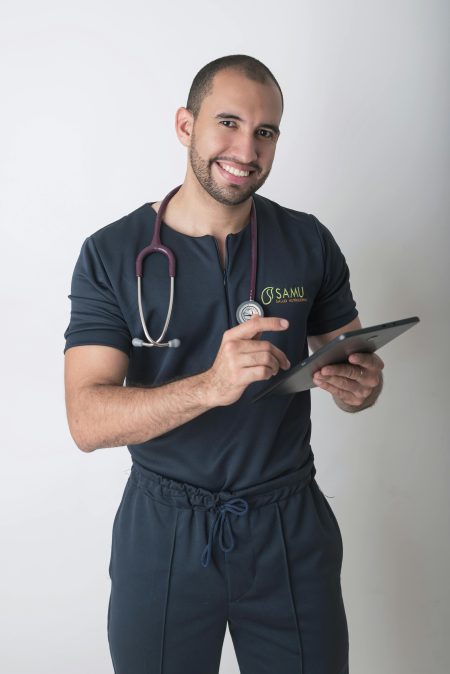 Young male doctor with a stethoscope using a tablet indoors, showcasing modern healthcare technology.