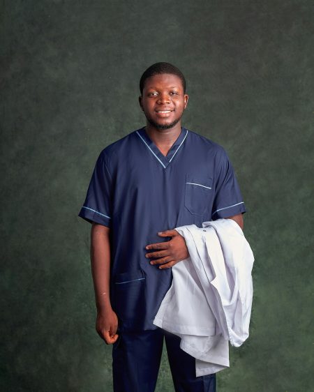 Smiling male nurse holding white coat with green background, professional healthcare portrait.