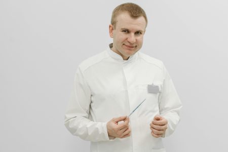 Smiling doctor in a white coat holding a medical instrument against a plain background.