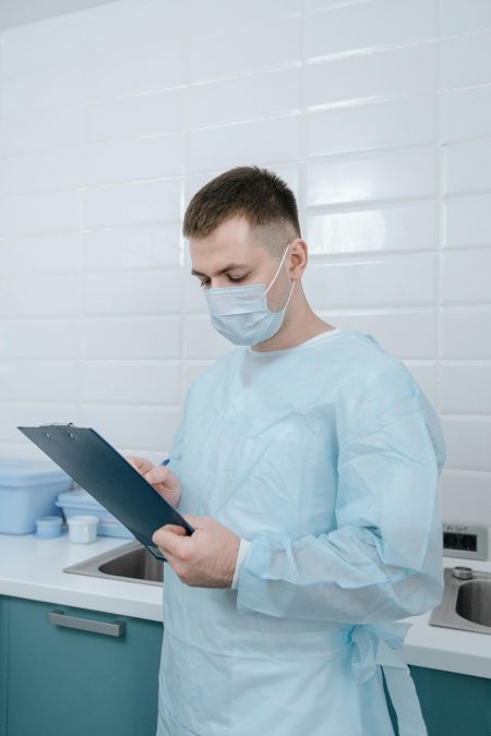 Medical professional in scrubs using a clipboard in a clean laboratory setting.