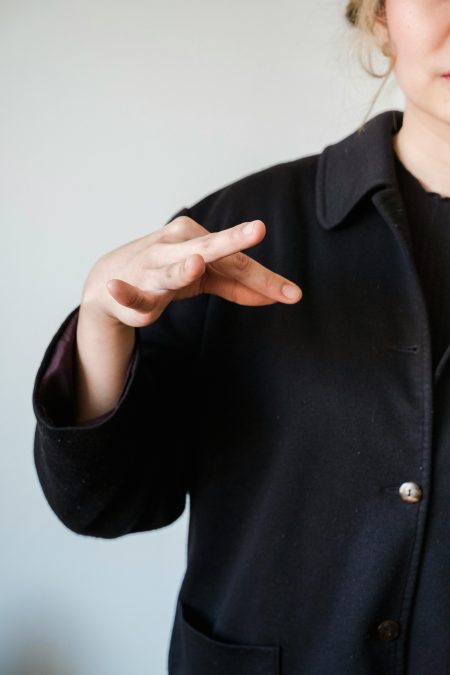 A close-up image showing a woman in a black coat using sign language, indoors.