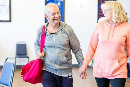 Happy senior couple holding hands and smiling in a gym setting, wearing casual sports clothing.