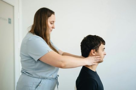 A physiotherapist performs a neck adjustment on a male patient in a clinic setting.