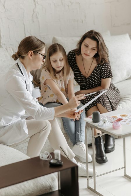 Doctor discussing health care plan with mother and daughter on sofa.